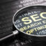 Magnifying glass and many words over black background, with the text SEO (Search Engine Optimization) written with golden letters. Internet marketing and SEO concept